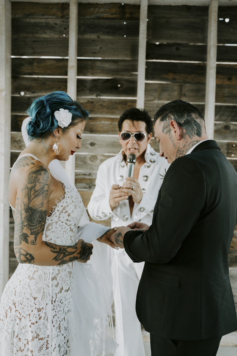 groom putting ring on hand of bride with blue hair 