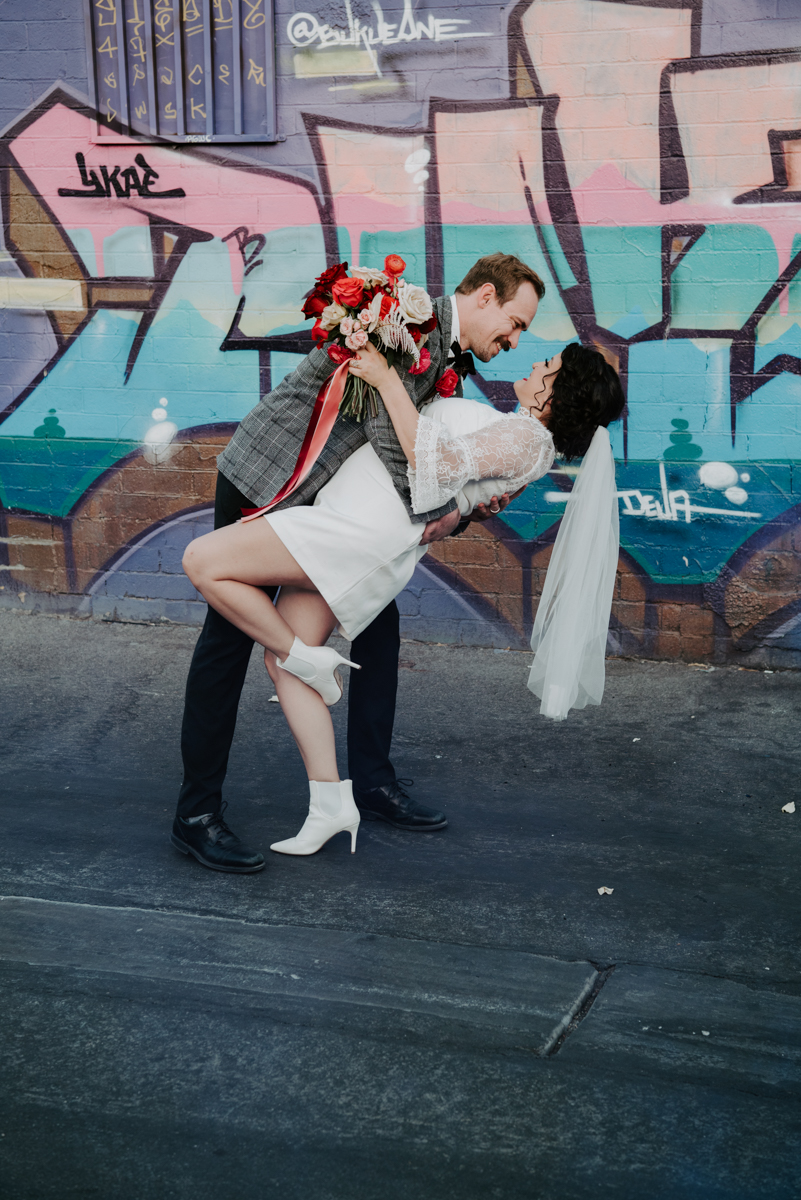 groom dipping bride in front of graffiti wall