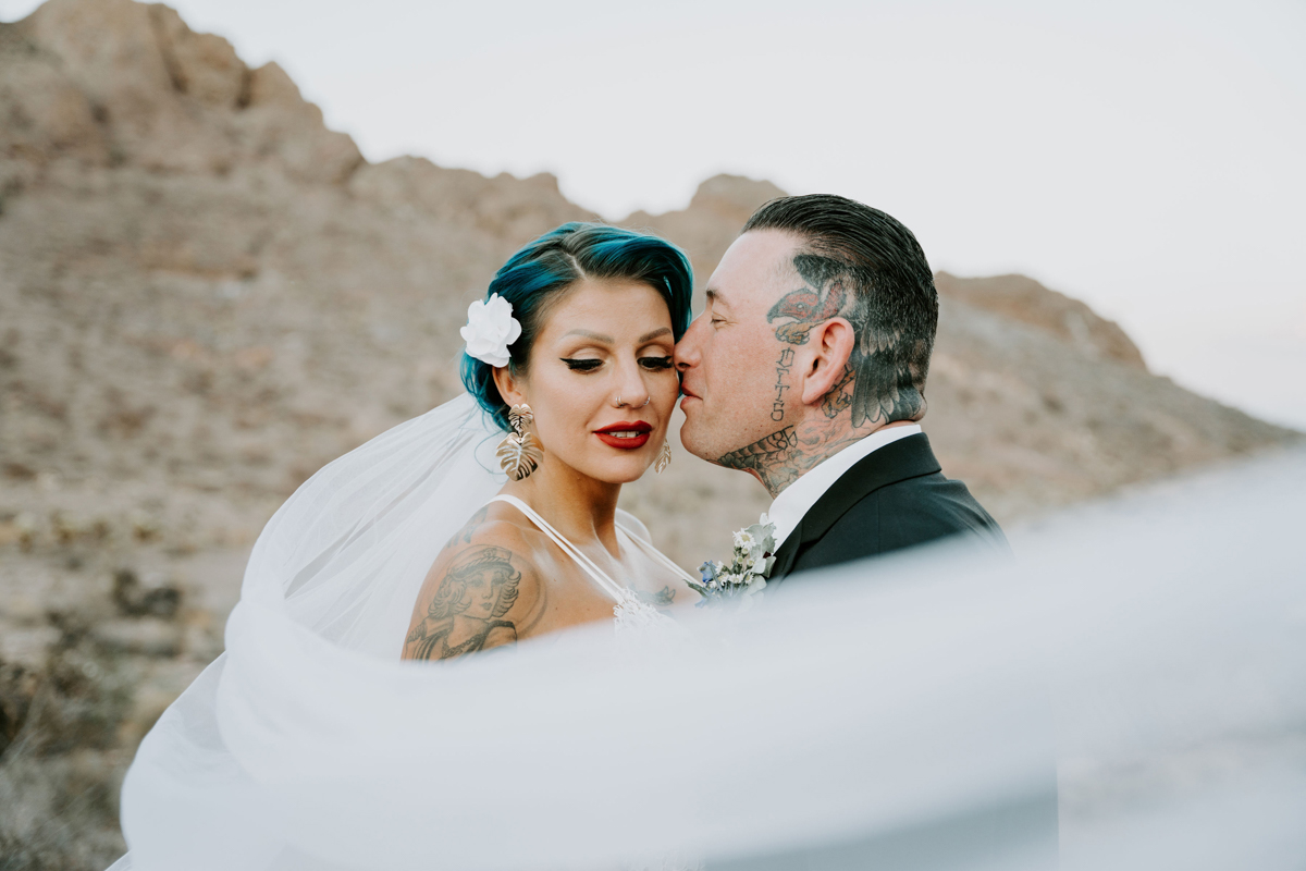 blue haired bride with tattooed groom and white veil wrapping around them