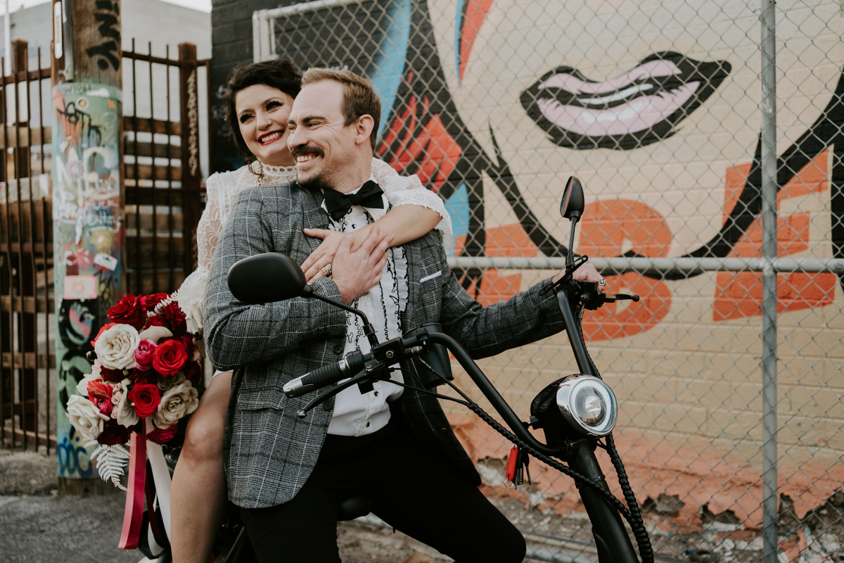 bride on back of moped driven by groom with graffiti in the background