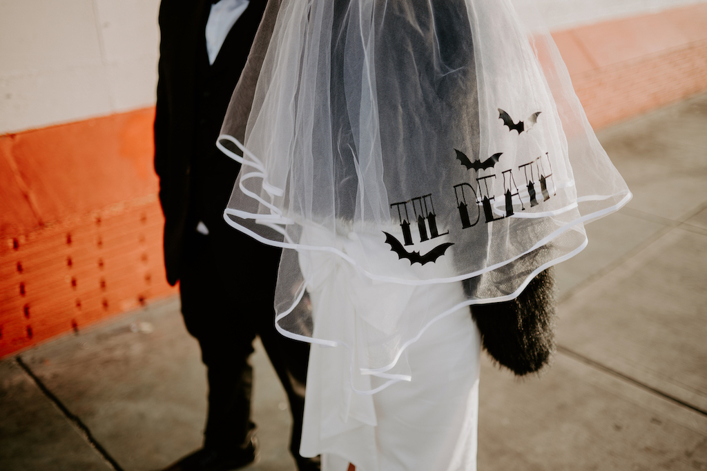 bride's dress and veil with image of black bats and the text 'til death' printed on the veil